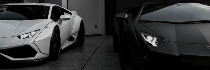 two sports cars parked next to each other in front of a garage door, one is white and the other is black