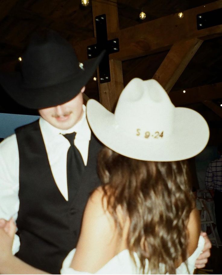 a man in a cowboy hat is dancing with a woman wearing a white dress and black vest