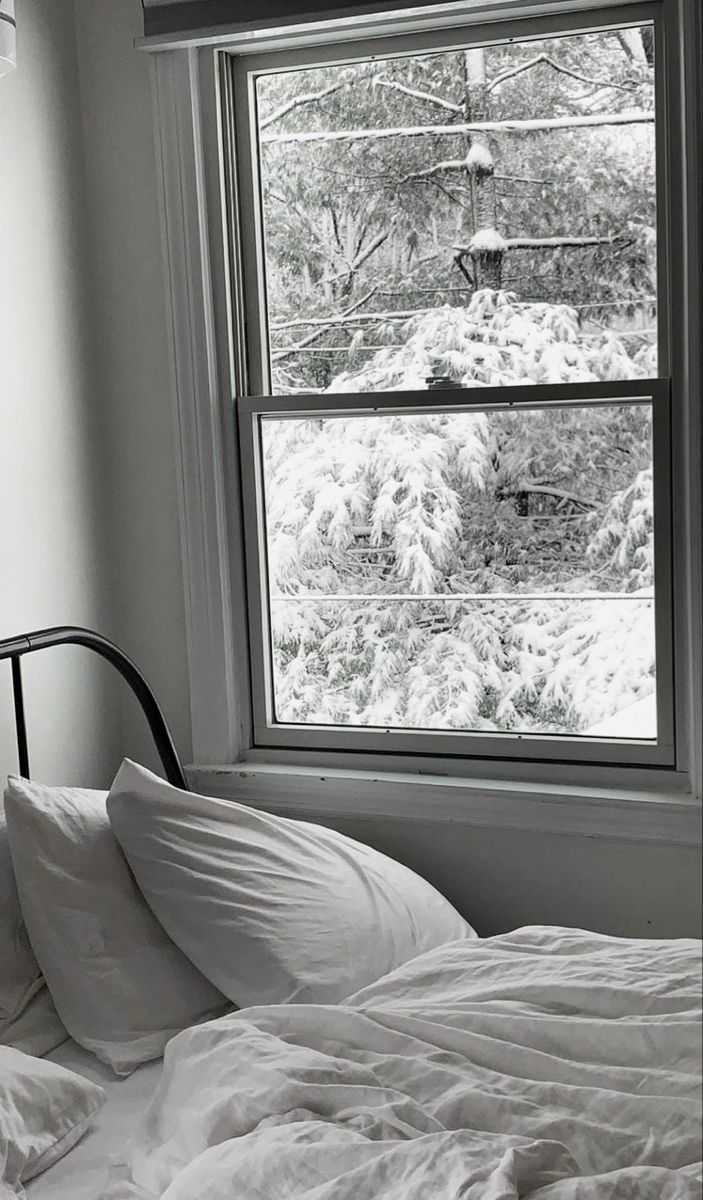 an unmade bed in front of a window with snow on the ground and trees outside