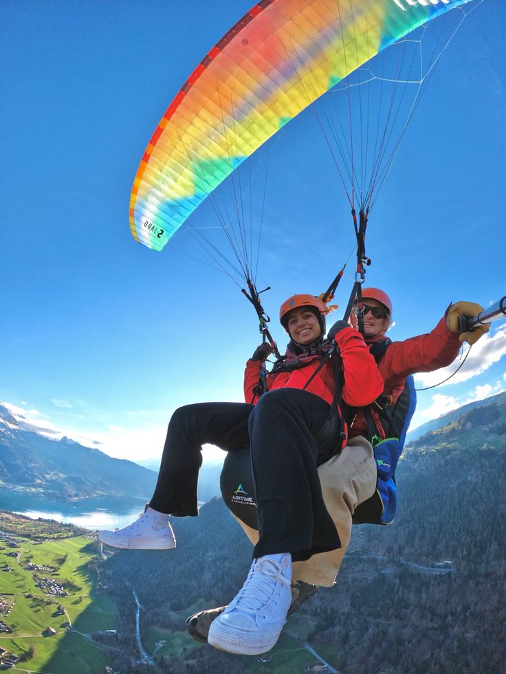 two people are parasailing in the mountains on a sunny day with colorful parachutes