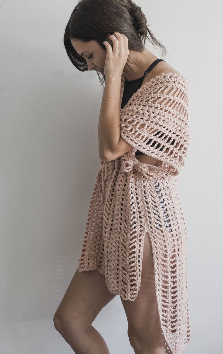 a woman standing in front of a white wall talking on a cell phone while wearing a crocheted shawl