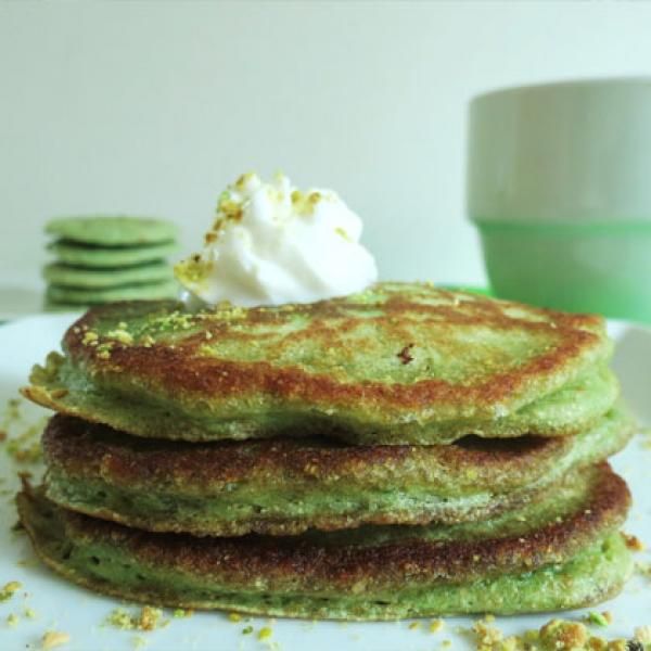 a stack of green pancakes on a plate with whipped cream and pistachio sprinkles