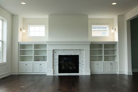 an empty living room with white bookcases and a fireplace