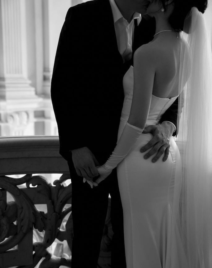 a bride and groom kissing in front of an ornate balcony at their wedding reception, black and white photograph