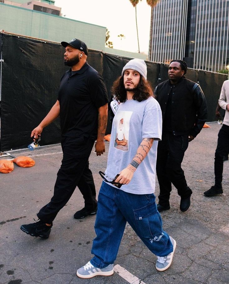 a man with long hair walking down the street in front of other men wearing black shirts and jeans