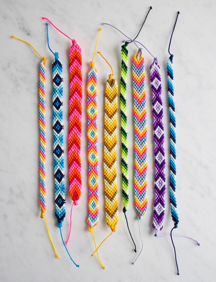 four colorful braided bracelets are lined up on a marble surface with string attached to them