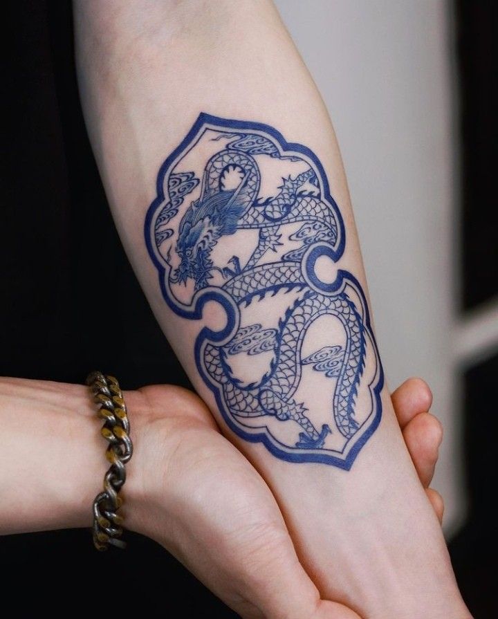 two hands holding each other with tattoos on their arm and wrist, one has a blue dragon in the middle