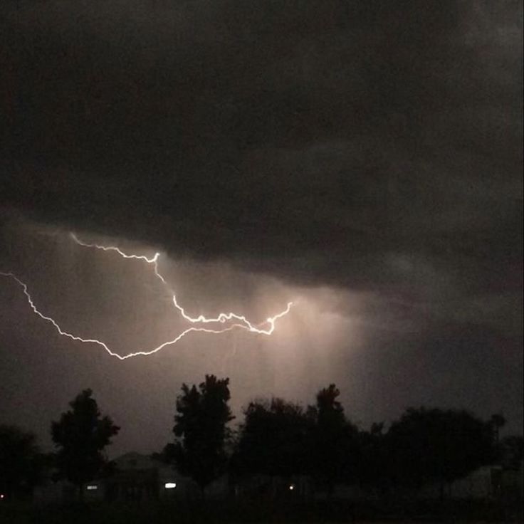 a lightning bolt is seen in the sky above some trees and houses on a cloudy night