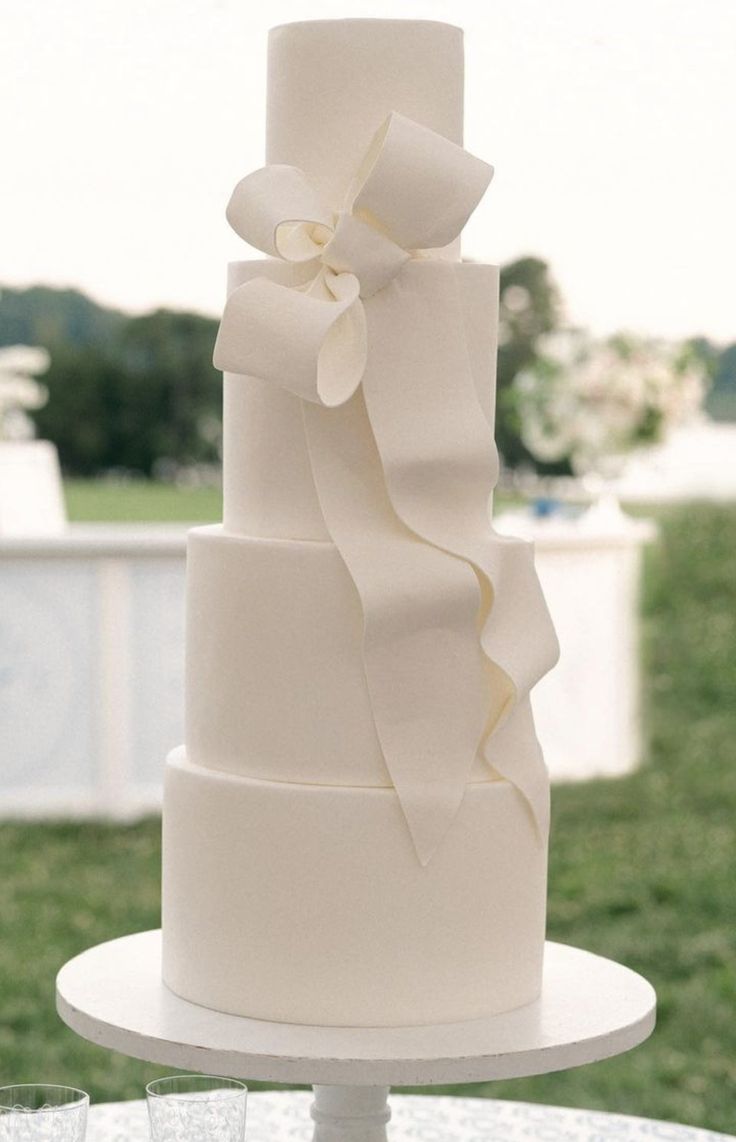 a three tiered white wedding cake sitting on top of a table next to wine glasses