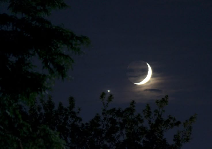 the moon and venus are visible through the clouds in the night sky above some trees