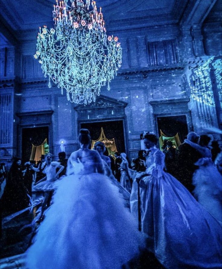 a group of people dressed in wedding gowns and dresses are dancing together with chandeliers hanging from the ceiling