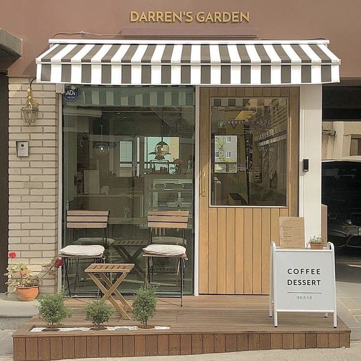 the outside of a coffee shop with two chairs and a sign in front of it