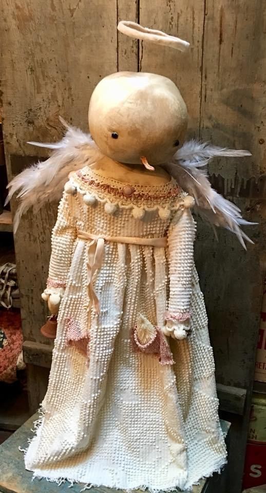 an old fashioned doll with feathers on it's head and dress made out of fabric