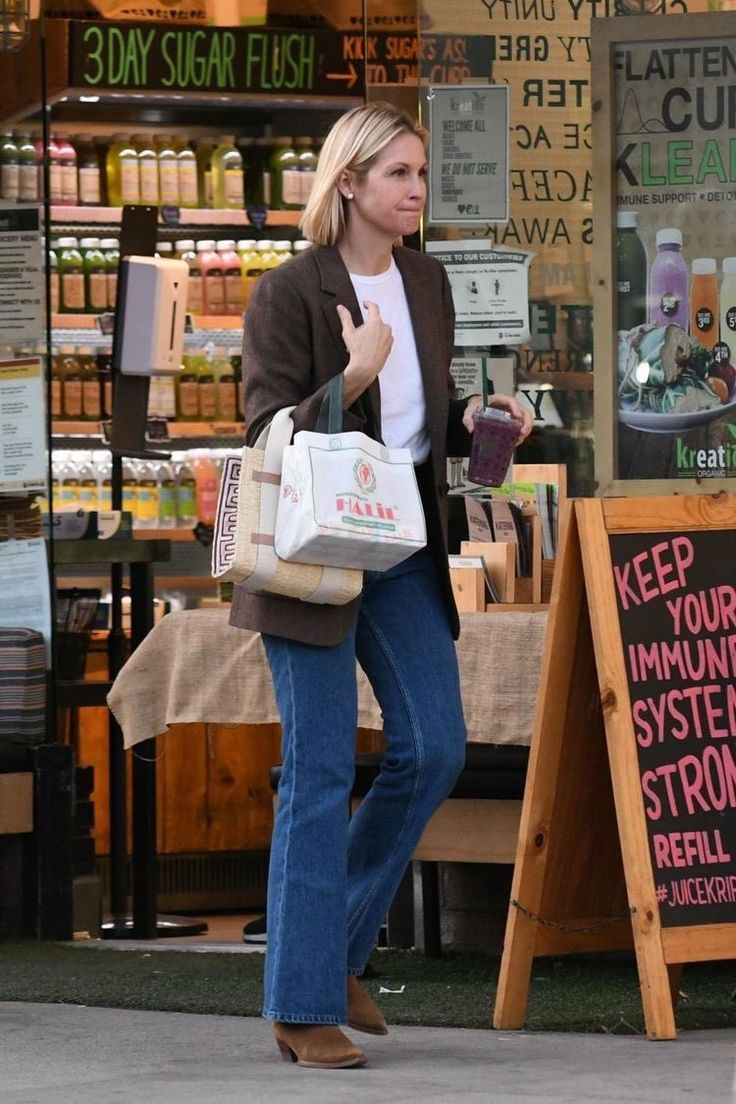 a woman is walking past a store with her hand in her pocket and holding a bag