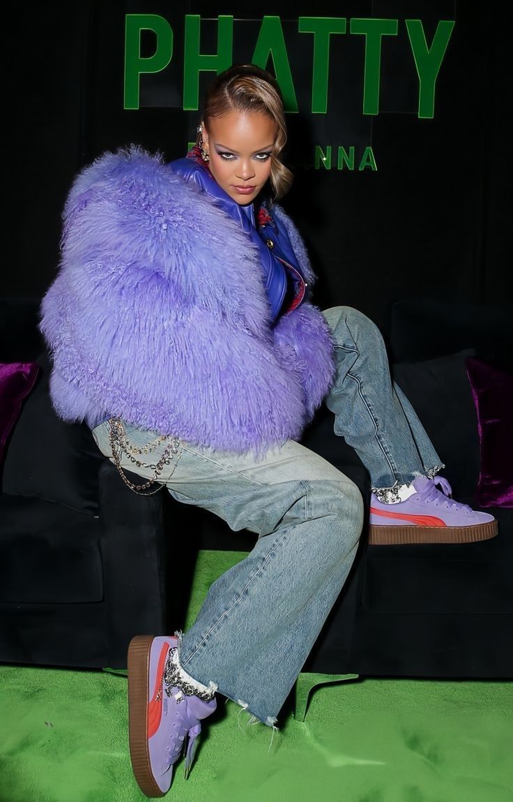 a woman sitting on top of a couch wearing purple furry coat and jeans with pink sneakers