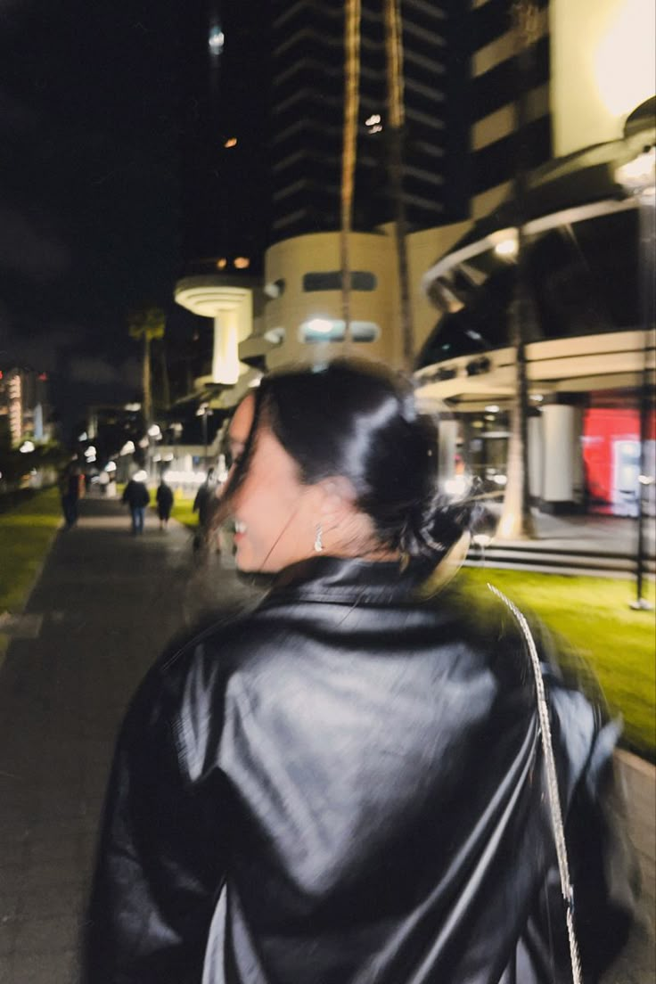 a woman walking down the street at night with her hand on her hip and looking off into the distance