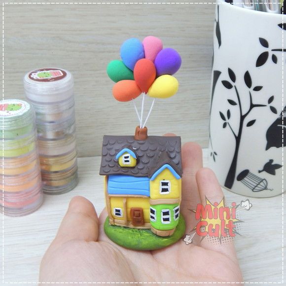 a hand holding a small toy house with balloons on the roof and in the air