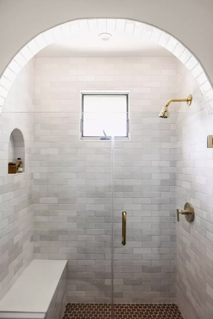 a white tiled shower with gold fixtures and a window