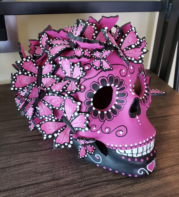 a pink and black skull with flowers on it's head sitting on a table