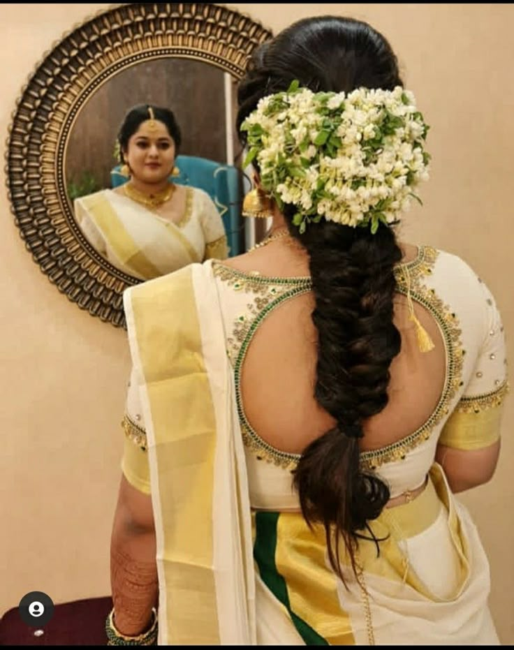 a woman with flowers in her hair is looking at herself in the mirror while wearing a saree