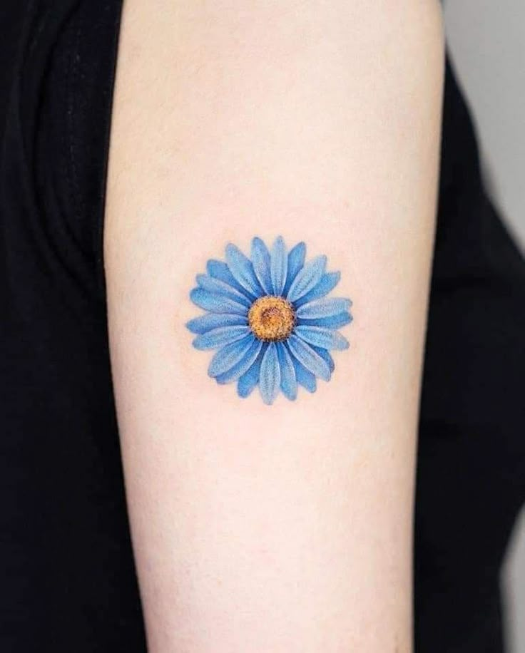 a blue flower tattoo on the left upper arm and shoulder, with an orange center