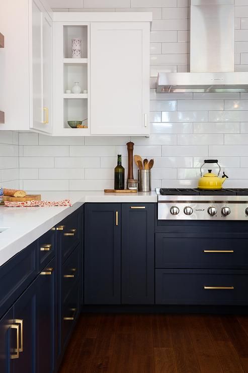 a kitchen with white and blue cabinets, wood flooring and brass pulls on the doors