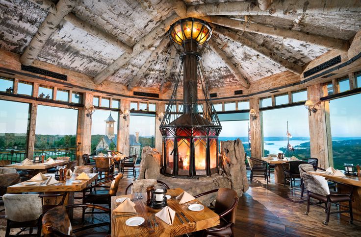 the inside of a restaurant with wooden tables and chairs, an open fire place in the center