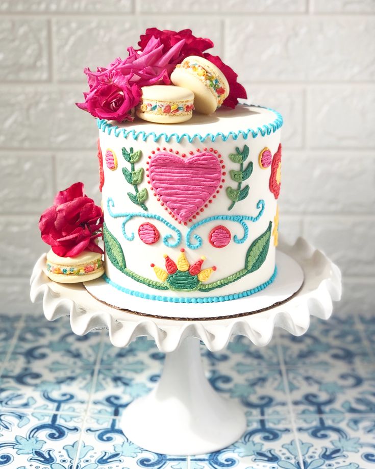 a decorated cake sitting on top of a white stand next to a blue and white tile wall