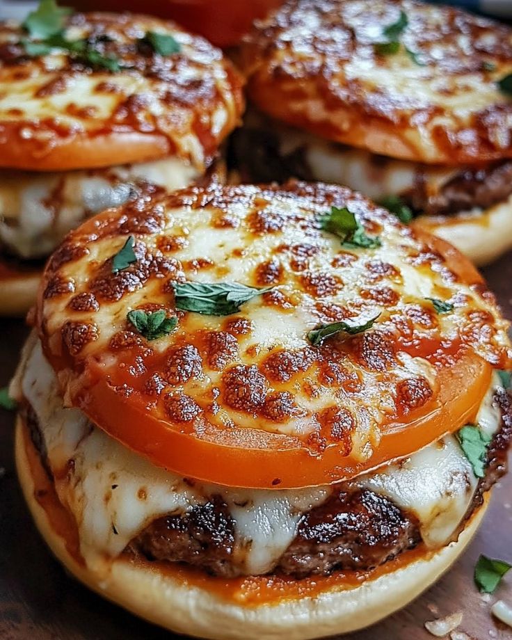 three cheeseburgers with tomato slices and basil