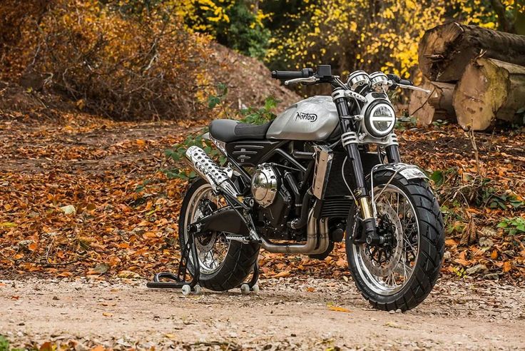 a motorcycle parked on the side of a dirt road in front of trees and leaves