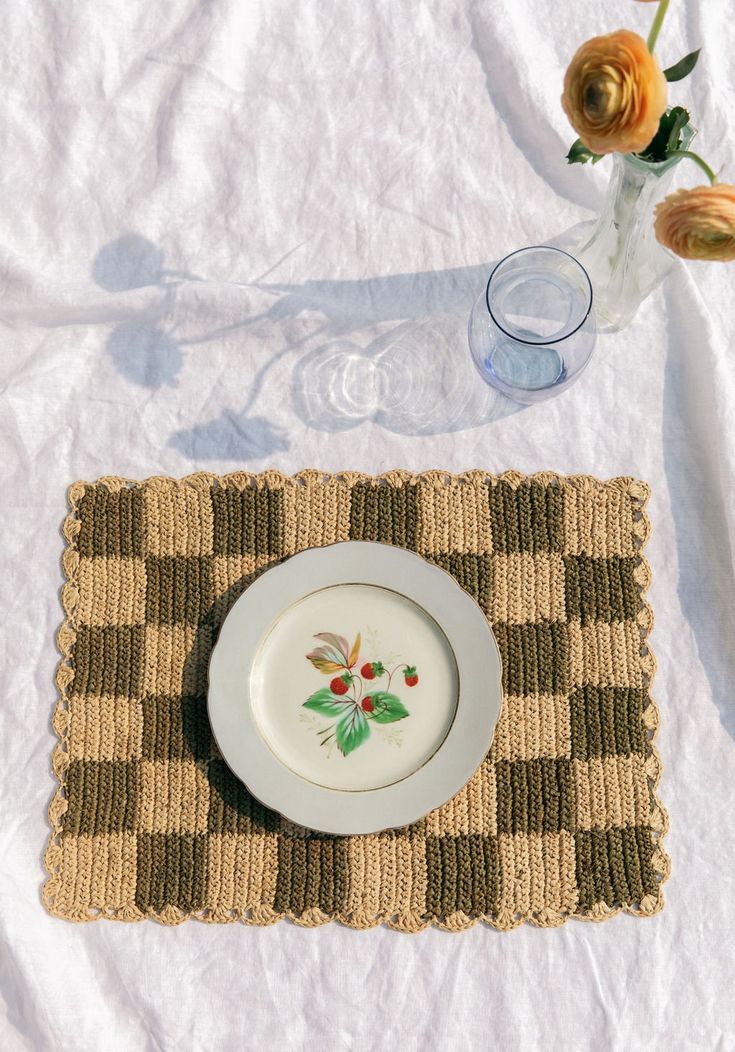 a place mat with a plate on it next to a glass vase and flower arrangement