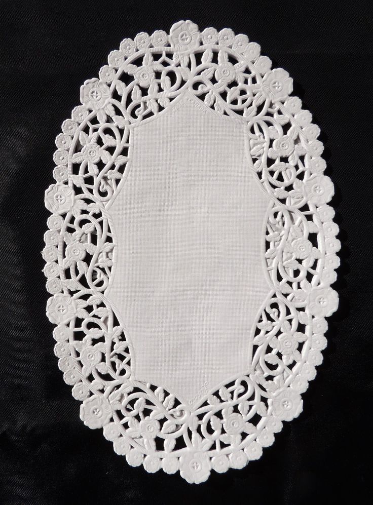 a white doily on a black background with an oval shape in the center and small flowers at the bottom