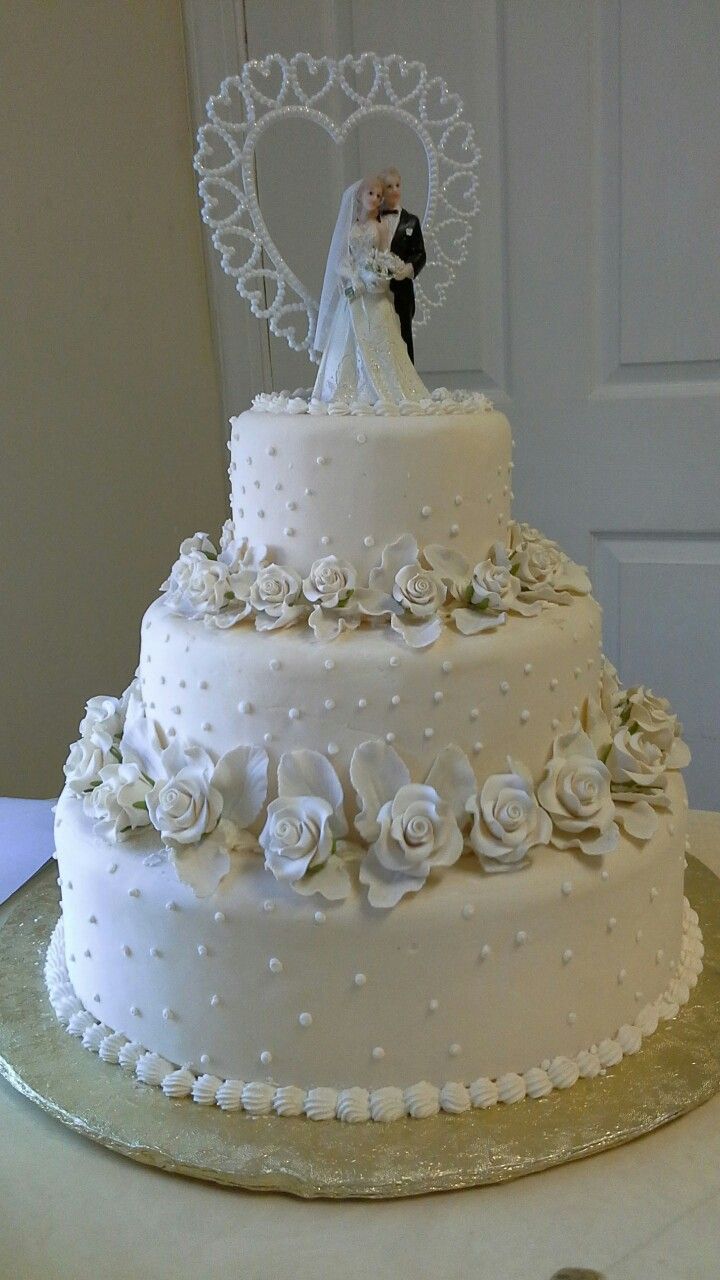 a wedding cake decorated with white flowers and a bride and groom on the top tier