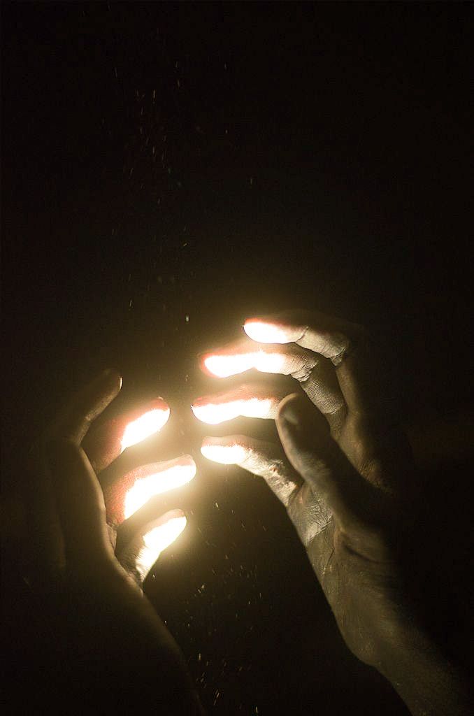 two hands holding lit candles in the dark