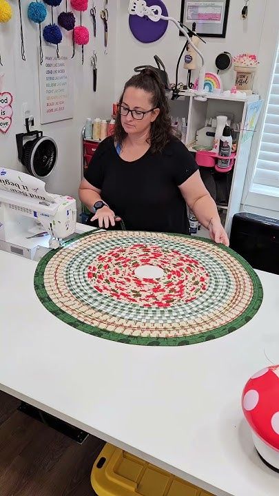 a woman sitting at a sewing machine working on a piece of art with red, white and green designs