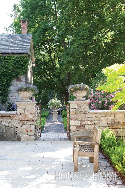 a wooden bench sitting in the middle of a garden next to a stone wall and trees