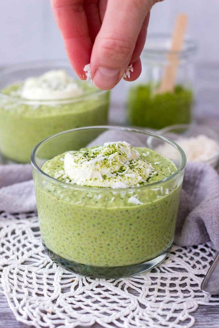 a person dipping something into a small glass bowl filled with green smoothie and whipped cream