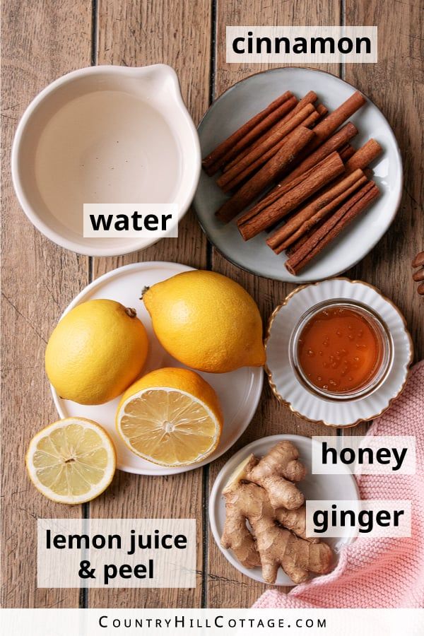 the ingredients to make lemon ginger tea on a wooden table with oranges and cinnamon