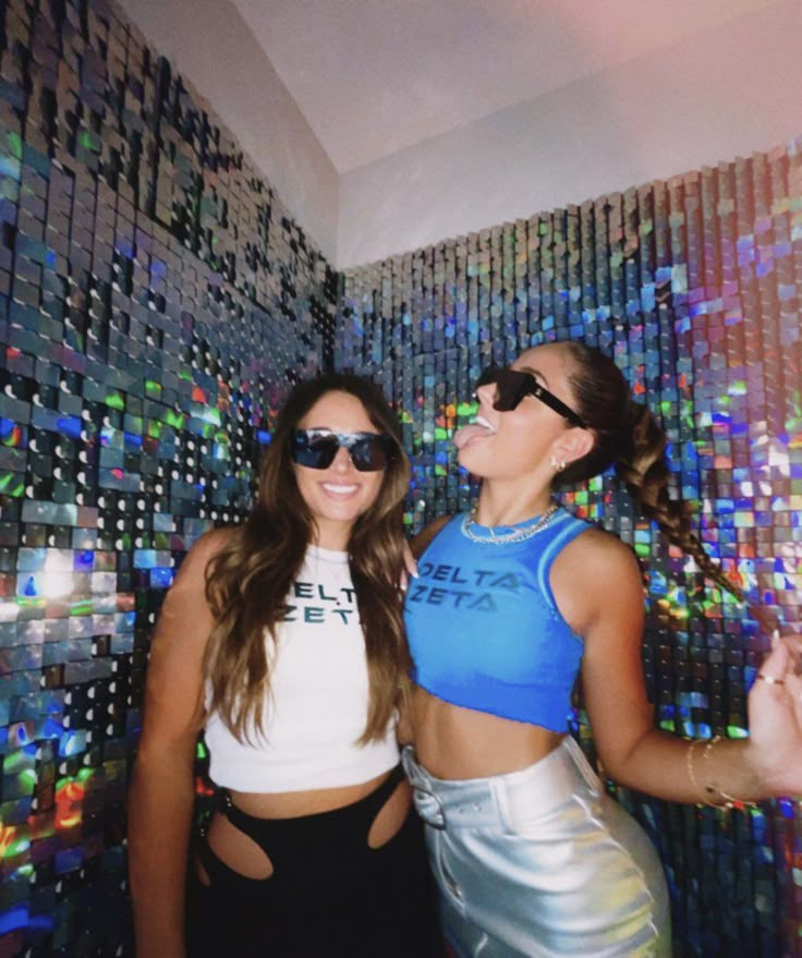 two young women standing next to each other in front of a wall covered with disco balls