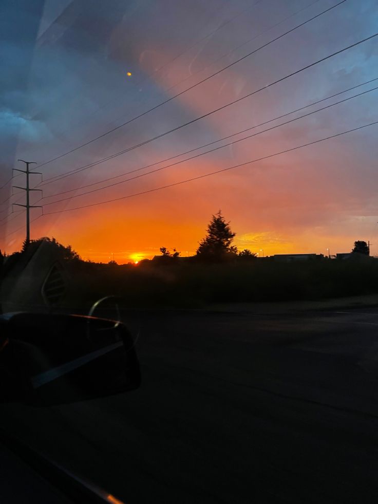 the sun is setting behind some power lines and telephone poles as seen from a car window