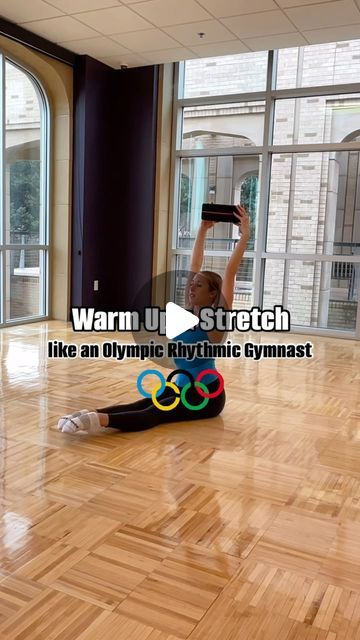 a woman is sitting on the floor with her hands up in the air and holding an olympic ring