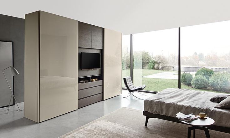 a bedroom with large windows and a television on the wall next to a bed in front of a sliding glass door