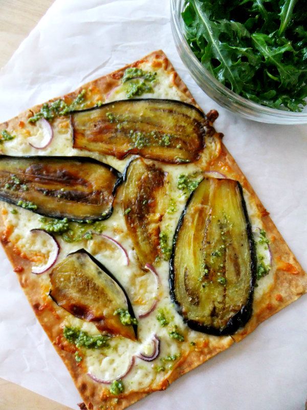 a square pizza with vegetables on it next to a bowl of greens and a salad