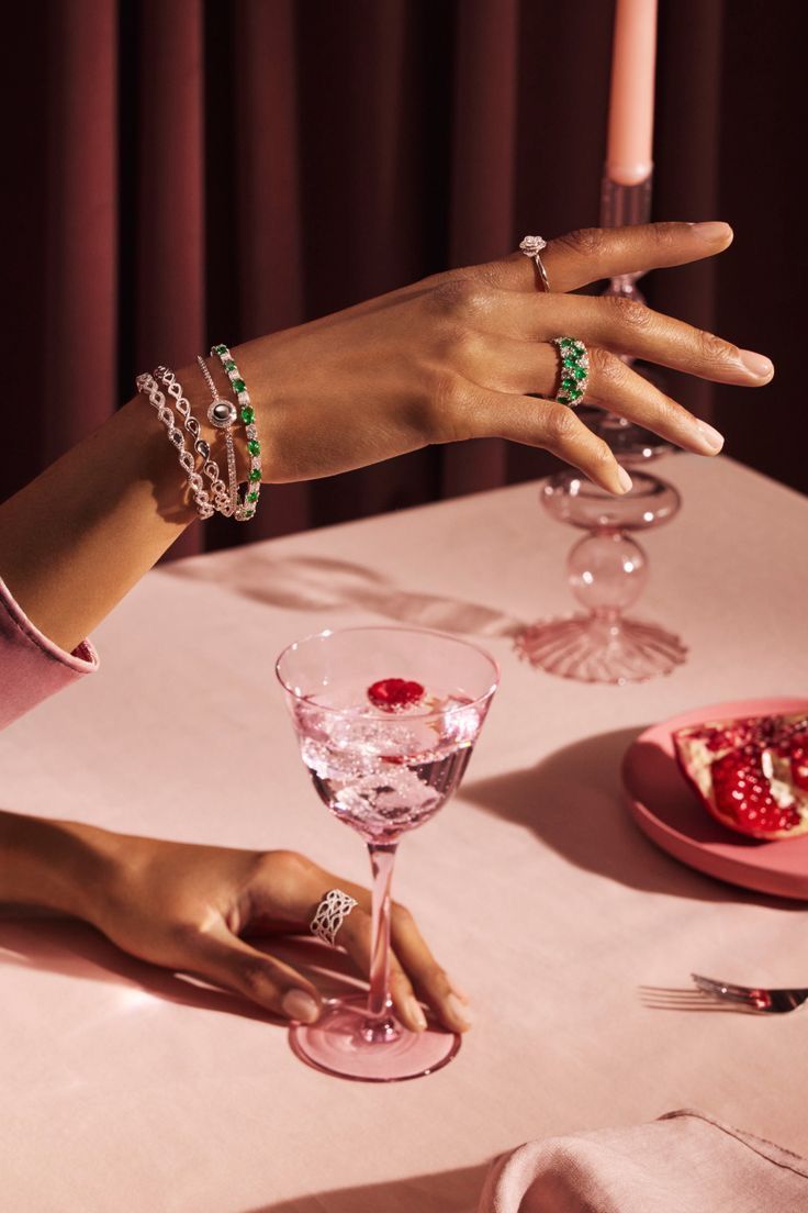 two hands holding wine glasses on top of a table with food and candles in the background