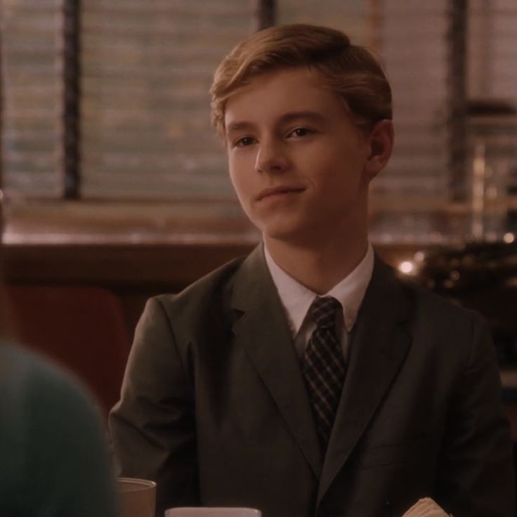 a young man in a suit sitting at a table with a coffee cup and saucer