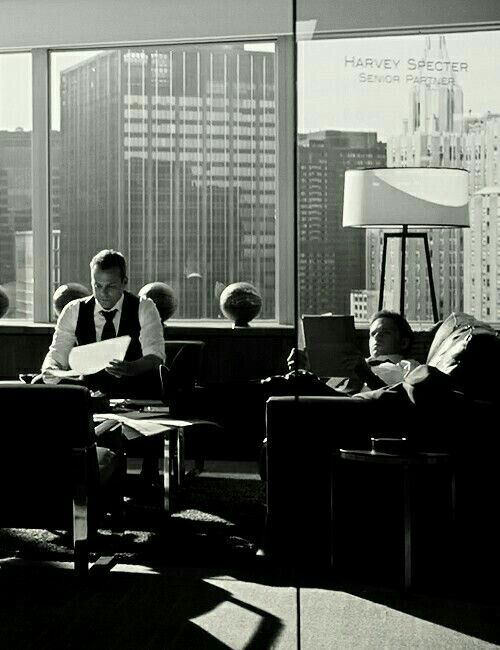 black and white photograph of people sitting at desks in an office with large windows