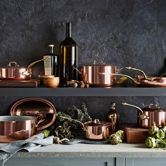 copper pots and pans are lined up on a shelf in front of a wine bottle