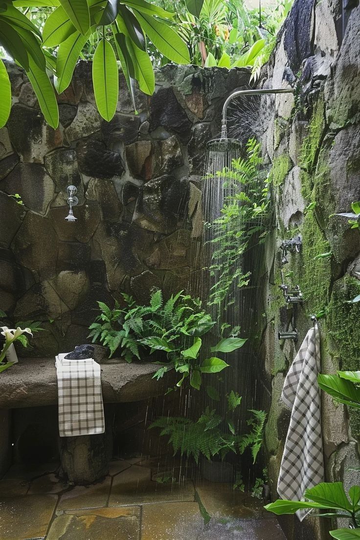 an outdoor shower is surrounded by greenery and rocks, with a bench in the foreground