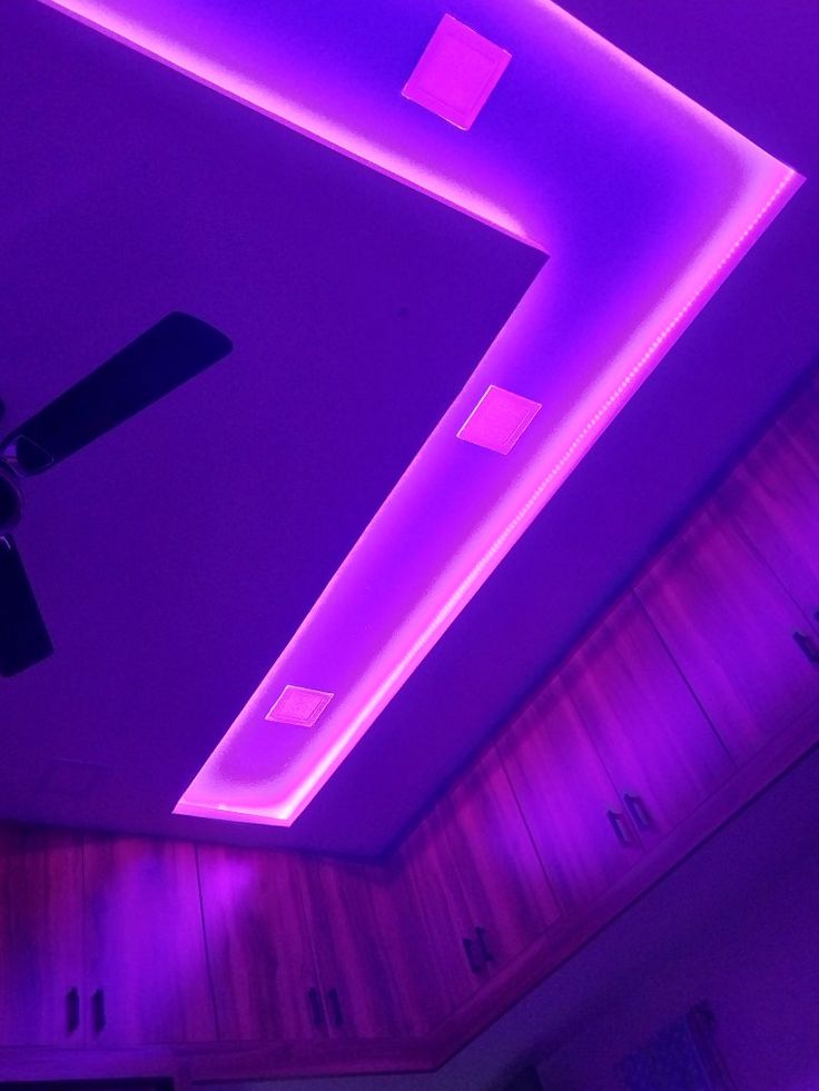 a ceiling with purple lighting and wooden cabinets in the corner, along with a fan