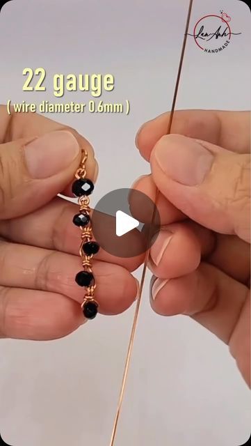 two hands are working on a beaded bracelet with black beads and gold plated wire